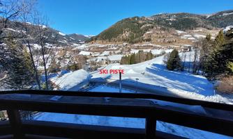 View of a snowy landscape with a ski slope. In the background, there are hills and trees visible.