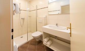 A modern bathroom with a shower, a sink, and a toilet. There are fresh towels and a clear, bright room available.
