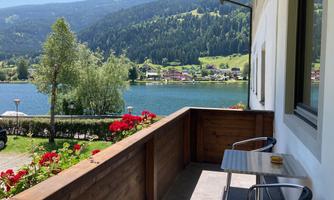 A beautiful balcony overlooking a clear lake and green mountains. Colorful flowers and a table with chairs complete the relaxed atmosphere.