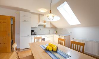 A bright kitchen with modern furnishings and a large window area. Fresh lemons are on the table in a bowl.