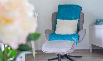 A cozy armchair with a blue blanket and a cushion. In the background, fresh flowers and bright room decor can be seen.