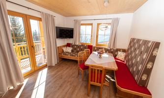 A cozy living space with wooden details, a dining area, and large windows. The furniture is in warm colors and creates an inviting atmosphere.