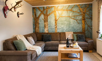 A cozy living room with a big couch and a wooden table. On the wall, there is an artistic tree landscape.