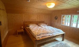 A cozy bedroom with wooden paneling and a large double bed. Large windows ensure plenty of light and an inviting atmosphere.