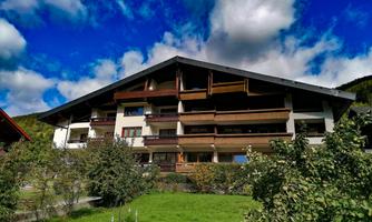 A modern building with several balconies in a green environment. The sky is blue with some clouds.