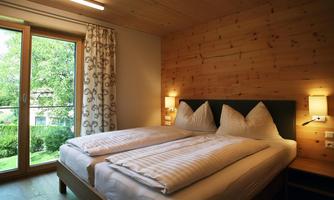 A cozy bedroom with two single beds and wooden paneling. Large windows provide a view of the garden and ensure plenty of daylight.