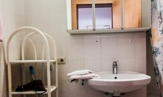 A small bathroom with a round sink and a mirror. On the wall, there is a shelf with towels and toiletries.