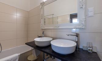 A modern bathroom with two round sinks and a large mirror. The walls are brightly tiled and there is a cozy bathtub.