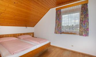 A cozy bedroom with a double bed and light wood. The window has colorful curtains and offers a view outside.