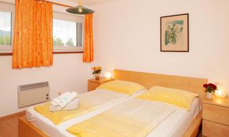 A bright bedroom with two beds and yellow bedding. The windows are decorated with orange curtains and there is pretty wall art.