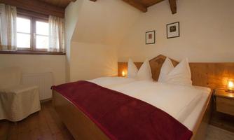 A cozy bedroom with two beds and a wooden design. Soft light and curtains on the windows create an inviting atmosphere.