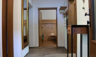 A bright hallway with wooden flooring and several doors. Mirrors hang on the wall and a small table is ready.