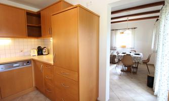 A modern kitchen with wooden cabinets and appliances. In the background, a cozy dining area is visible.