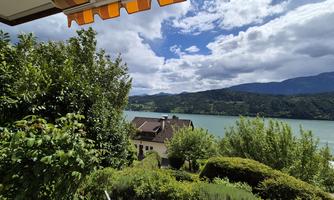 A picturesque view of a lake, surrounded by green trees and mountains. The sky is partly cloudy, creating a relaxing atmosphere.