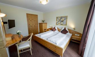 A modern hotel room with two single beds and a desk. The walls are in soft colors, and there are decorative elements such as a picture and a plant.
