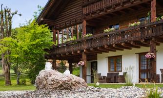A traditional wooden house with a beautiful balcony and blooming plants. In the foreground, there is a decorative stone with a small water jet.