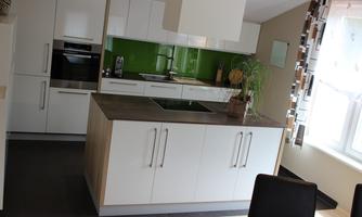 A modern kitchen with white cabinets and a green wall. In the foreground is a kitchen island with a cooktop.