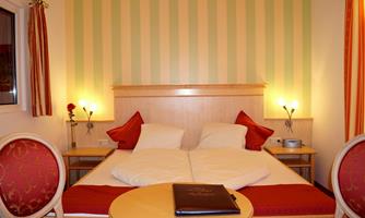 A cozy bedroom with a double bed and colorful striped walls. In the foreground, there are two chairs and a table.