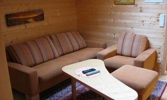 A cozy seating area with a brown sofa and a chair. The room has wood-paneled walls and a carpet.