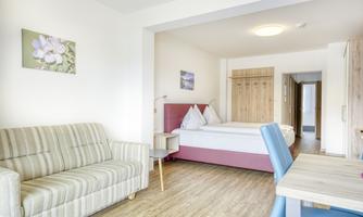 A bright and modern room with a cozy sofa and a double bed. The decor is friendly and inviting, ideal for a relaxing stay.
