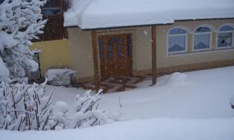 A snow-covered house with a beautifully designed entrance area. The snow lies thick on the ground and the plants.