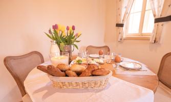 A beautifully set breakfast table with fresh rolls and a bouquet of tulips. In the background are glasses, eggs, and a milk jug.