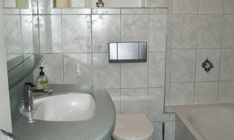 A small bathroom with a sink, a toilet, and a bathtub. The walls are tiled with light tiles, and there is a mirror above the sink.
