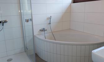 A modern bathroom with a comfortable bathtub and a separate shower. The walls are tiled with bright tiles, and a window provides natural light.