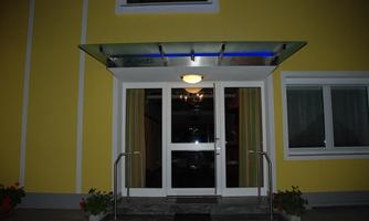 An inviting entrance to a building with a yellow facade. The entrance doors are made of glass and are sheltered by a canopy.