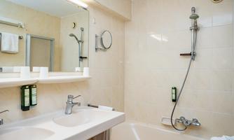 A modern bathroom with a bathtub and two sinks. Towels hang on the wall and toiletries are within sight.