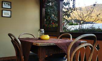A cozy dining area with a round wooden table and four chairs. In the background, there are windows with a view of nature.