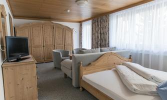 A cozy room with wooden furniture and plenty of natural light. There is a bed, a seating area, and a television.
