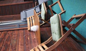 A cozy balcony with two wooden chairs and a table. A relaxing atmosphere with a reclining lounge chair and green carpet flooring.