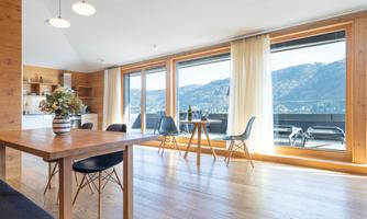 A modern living room with wood decor and large windows. The view overlooks the mountains and there is a small table with chairs.