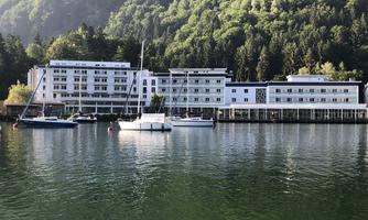 A modern building by the water, surrounded by lush greenery. Boats lie peacefully in the harbor.