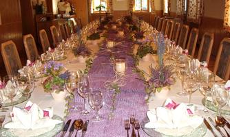 A festively set table in a cozy room. The table is adorned with purple table runners, flower arrangements, and elegant dishware.