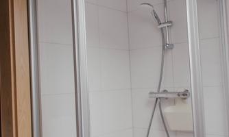 A modern shower enclosure with glass doors. The walls are tiled in white and the shower head is mounted on the wall.