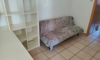 A simple room with a gray sofa and a white shelf. The floor is made of tiles and the walls are light.