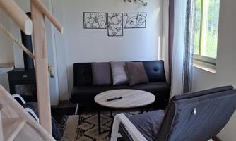A modern living room with a black sofa and a round table. Large windows let in plenty of light and create a pleasant atmosphere.