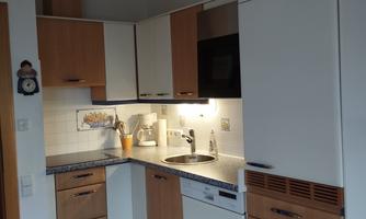 A modern kitchen with wood and white fronts. It is well equipped with a stove, a sink, and a dishwasher.