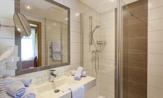 A modern bathroom with a shower and a large mirror. Clean towels are laid out on the sink.