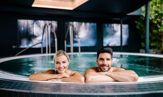 A couple relaxes in a hot tub. In the background, modern pictures and a calm atmosphere can be seen.