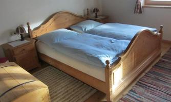 A cozy bedroom with a wooden double bed. The ceiling is covered with blue bed sheets, and there are nightstands on both sides of the bed.