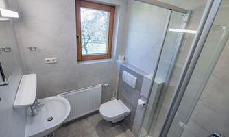 A modern bathroom with gray tiles. It has a shower, sink, and a window with a view outside.
