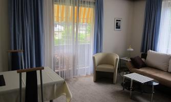 A cozy living room with a comfortable couch and a modern table. Large windows with blue curtains let in plenty of light.
