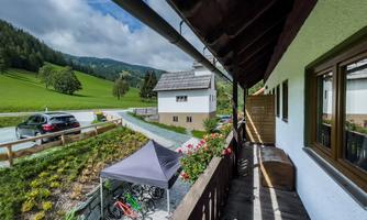 A view from the balcony into a green valley with a small house. In the foreground, there are flowers and bicycles.