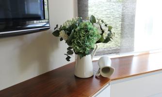 A beautiful bouquet of flowers in a white vase is on a wooden shelf. Next to it lies a small, white flower vase.