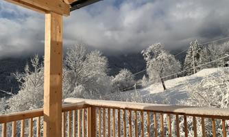 A snowy winter landscape with trees covered in snow. In the foreground is a wooden balustrade that offers a view of the winter scene.