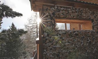 A stack of wood against the wall of a house in winter. The sun shines through the window, creating a calm, cozy atmosphere.