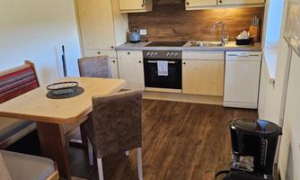 A modern kitchen with wooden-colored cabinets and a dining table. The room is bright and cozy furnished.